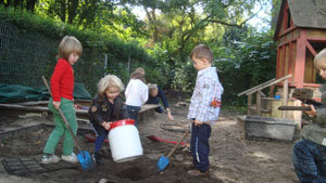 Ein Junge stellt eine weiße Kunstofftonne mit rotem Deckel in das Erdloch